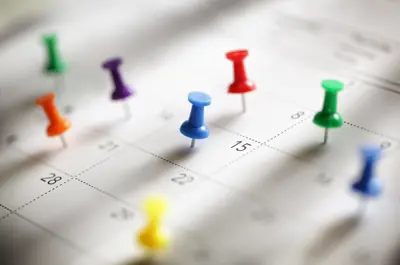 A close up of a calendar with colourful push pins on various dates.