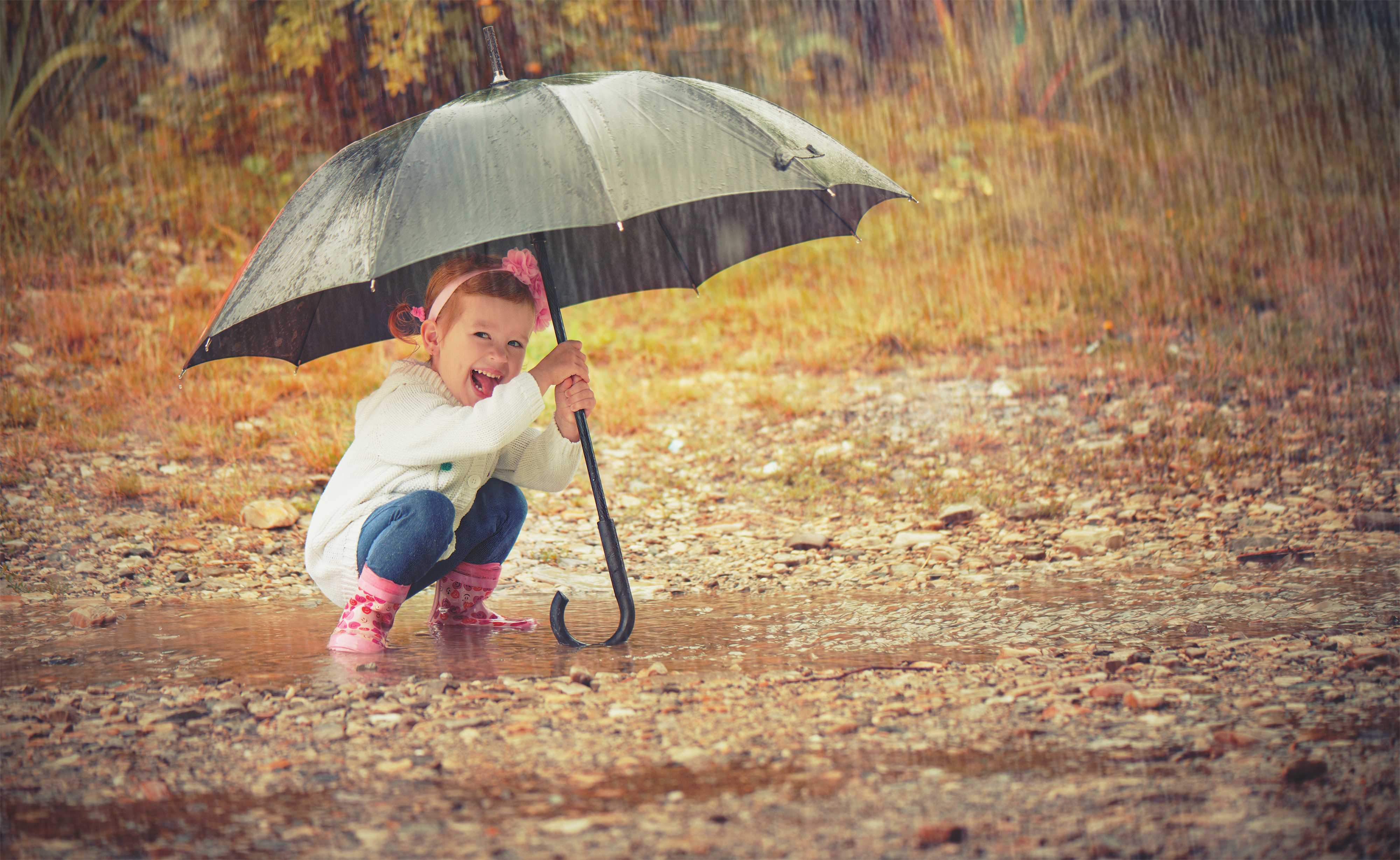 Girl smiling while crouching in a puddle holding a large black umbrella