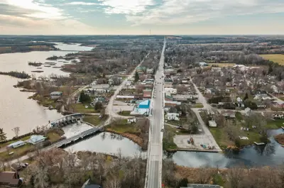 Aerial view of a town with buildings, trees and farm land in the distance. A main road runs down the middle.