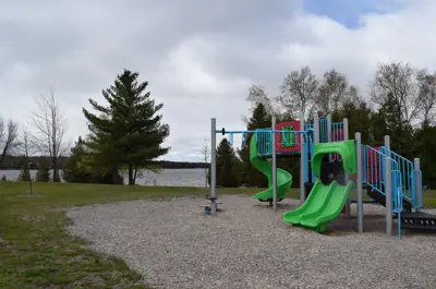 A multi-coloured playground with sand and a lake in the background with a few trees on the horizon.