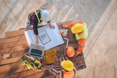 Aerial view of three construction workers wearing hard hats looking over a building plan