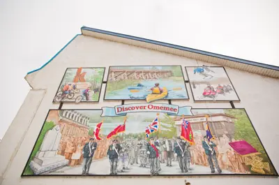 An art display with different Canadian scenes and a painted banner that reads Discover Omemee