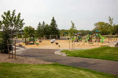 Playground with slides and swings next to a paved trail and trees nearby