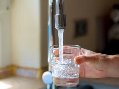 Someone holding a glass to a tap filling up with water
