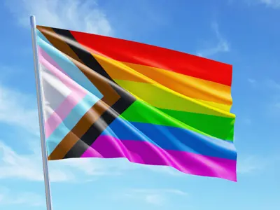 Image of Pride flag flying with a blue sky in the background.