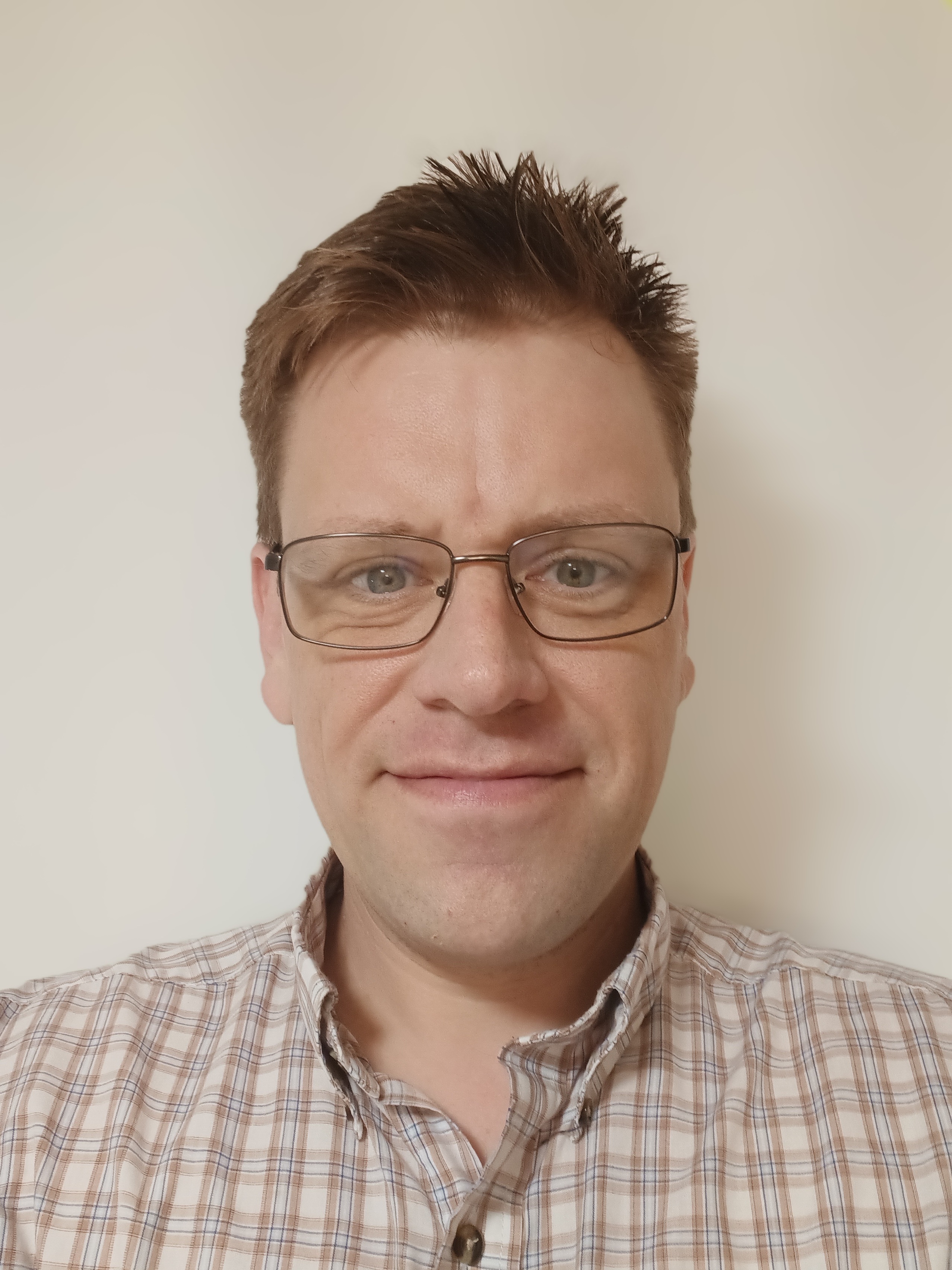 Male with short light brown hair and glasses, wearing a plaid shirt.