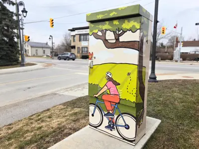 Photo of a traffic control box wrapped with an image of a person riding a bicycle. Streelights and a road are in the background.