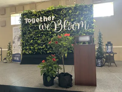 an empty stage with a podium and a large living wall behind it with the words "Together We Bloom"
