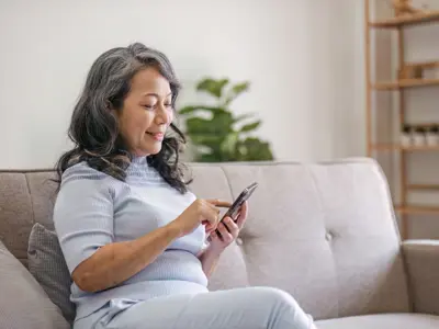 Woman sitting on a light coloured couch, using her phone. The photo illustrates how easy it is to 'Go Paperless.'