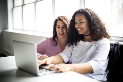 Two women sitting down, typing on a laptop