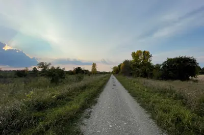 Gravel path through grassy area against a cloudy sunset