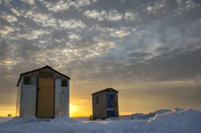 Two hunting shacks on a frozen lake at sunrise
