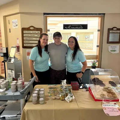Two women and an older man stand behind a table of baked goods.