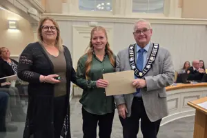 Photo of three people standing and facing the camera. The centre person is holding an envelope.