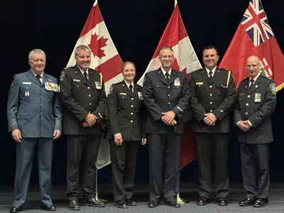 A group of uniformed paramedics pose on a platform in front of three flags as one person receives an award