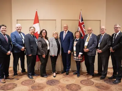 Photo of ten people in formal business clothes posed in a line in front of Canada and Ontario flags.