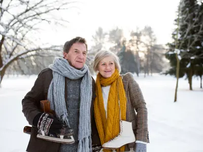 Elderly couple with winter attire with skates on their shoulders