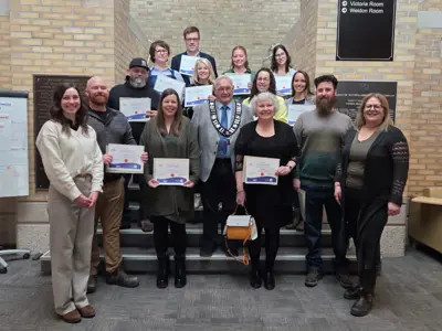 A group of six people are smiling and standing indoors on a staircase. The background is yellow brick.