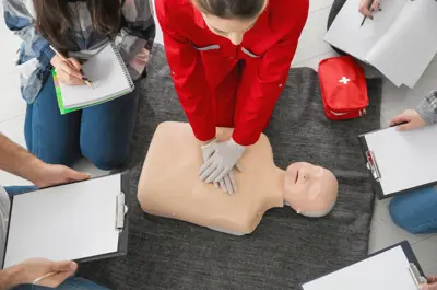 Aerial view of a CPR dummy with a woman demonstrating CPR to a small group of people with open notebooks