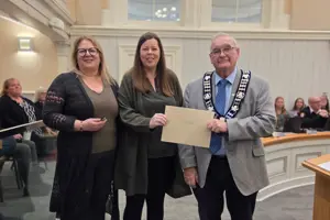 Photo of three people standing and facing the camera. The centre person is holding an envelope.