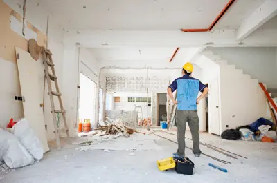 Man in hard hat standing facing an open room under construction.