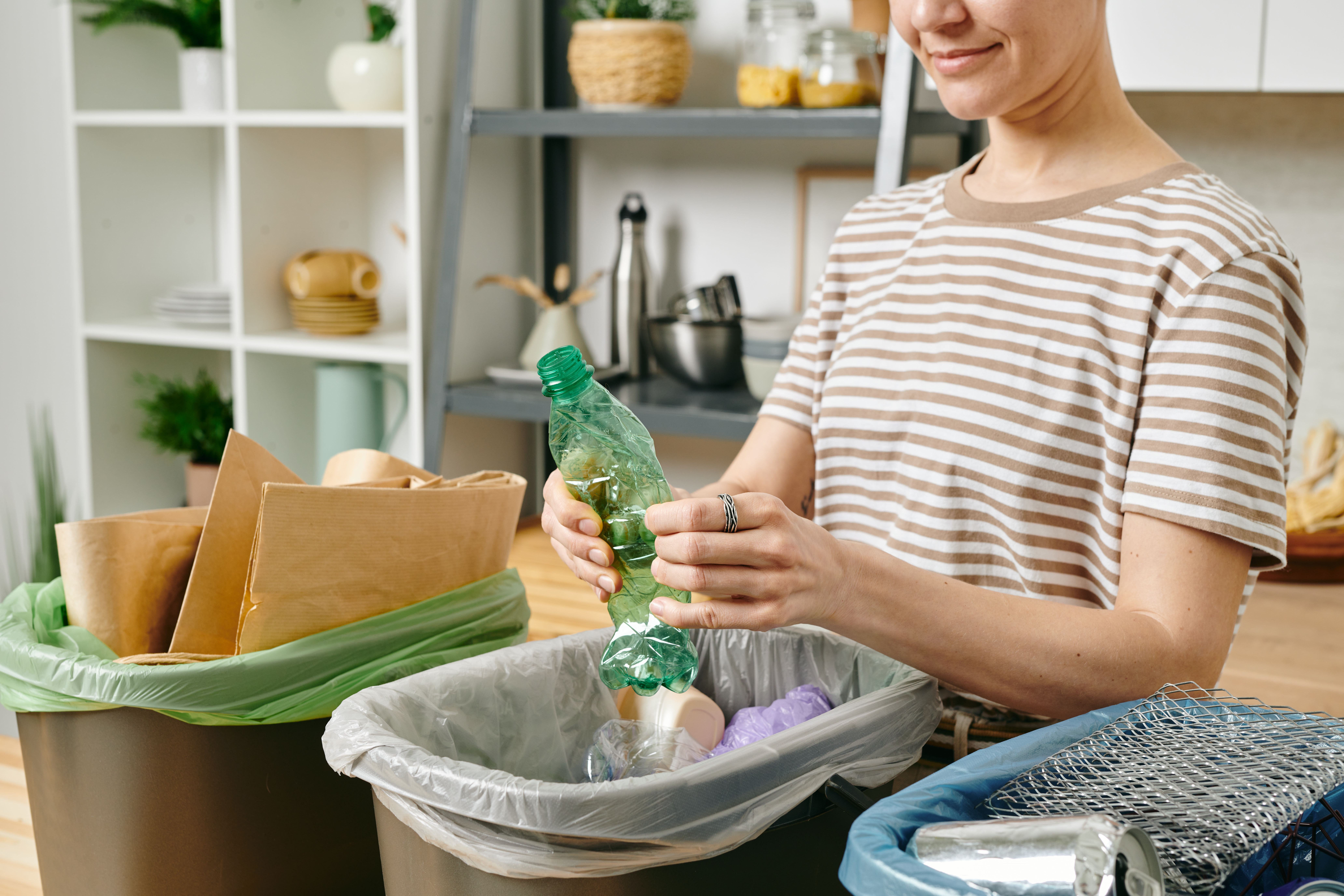 a person hold a plastic bottle hovering over three different bins of recyclable materials