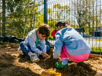 Photo of two children playing in a sandbox on a sunny spring day.