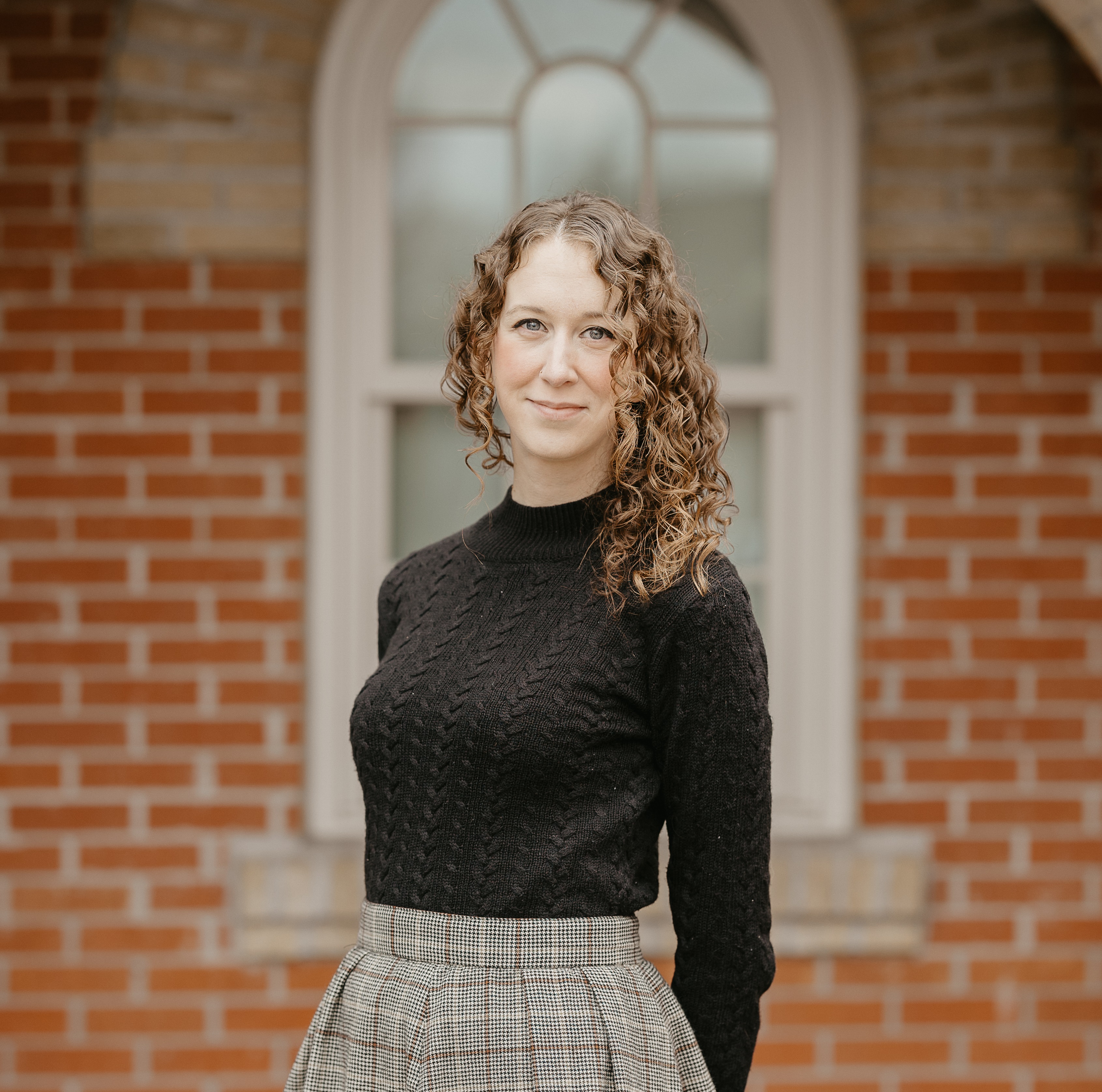 Woman with curly hair and wearing a black shirt stands in front of a brick wall.