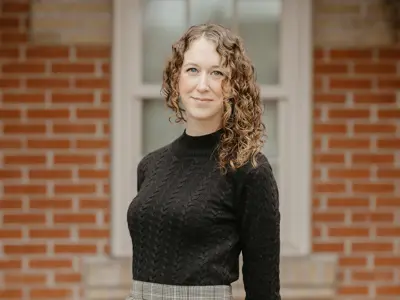 Woman with curly hair and wearing a black shirt stands in front of a brick wall.