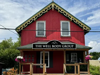 Red house with sign that reads The Well Body Group set against a blue cloudy sky