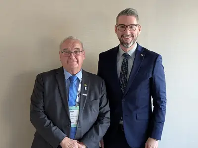 Two men wearing business suits face the camera and smile.