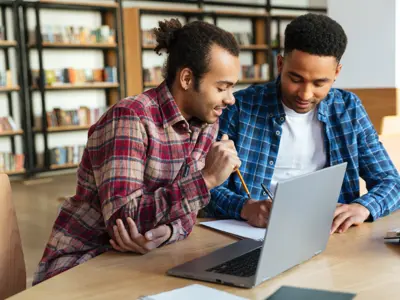 Two men sitting at a table looking at a laptop and a piece of paper