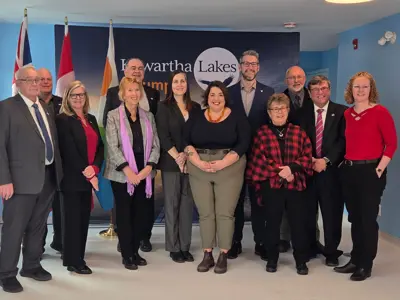 Photo of six men and six women standing posed in front of three flags and a Kawartha Lakes backdrop banner.