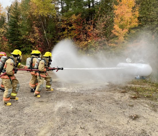 Volunteer firefighters shooting a water hose at a large residential propane tank in a contained training exercise