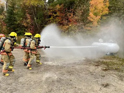 Volunteer firefighters shooting a water hose at a large residential propane tank in a contained training exercise