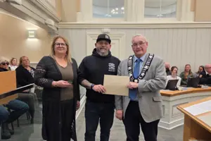 Photo of three people standing and facing the camera. The centre person is holding an envelope.