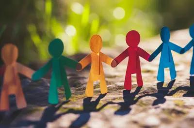 Paper cutout people linking hands on a brown surface with a green background