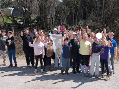 a group of children pose outside as a group with a garbage that contains trash they've collected