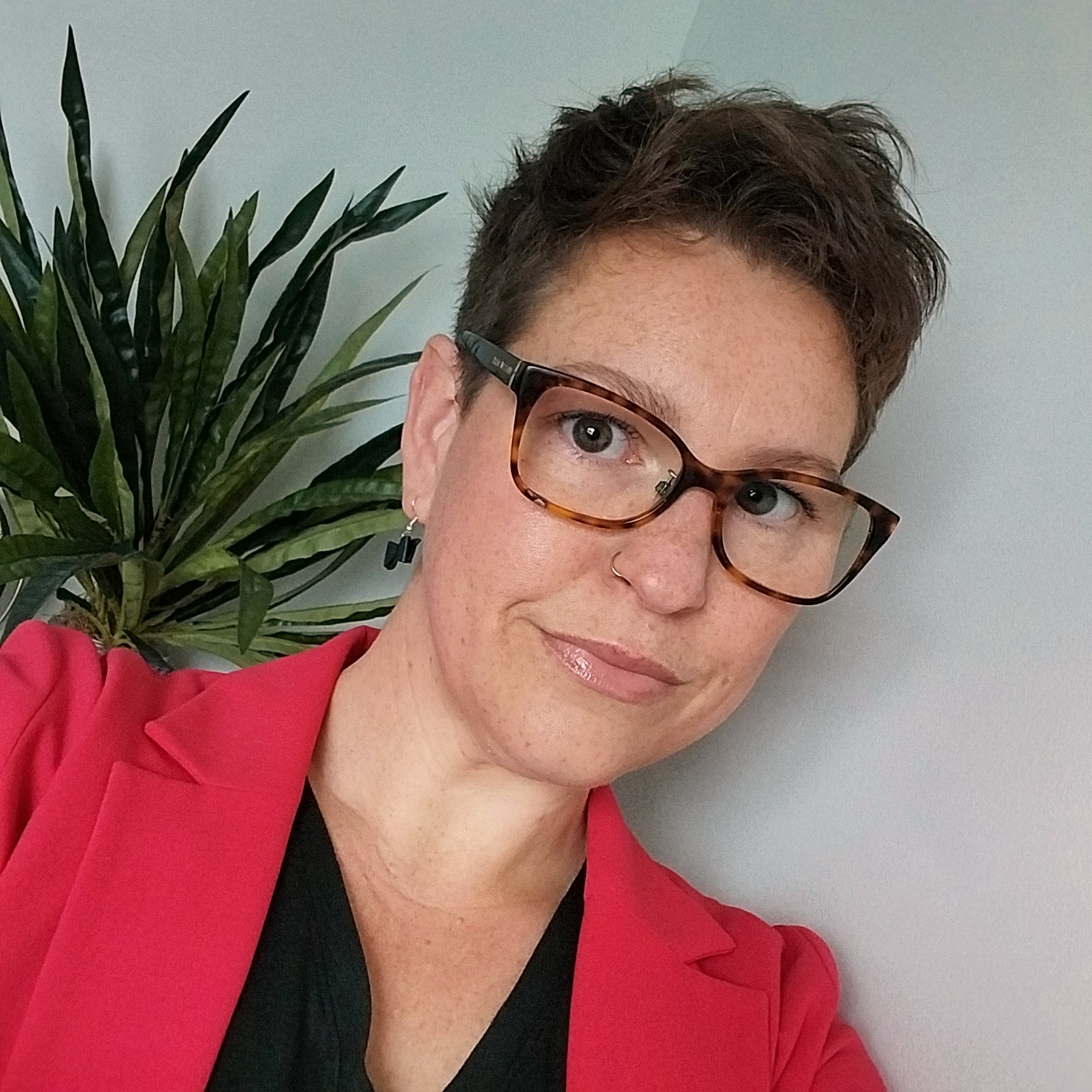 Female with short dark hear wearing glasses and a red blazer with black top.