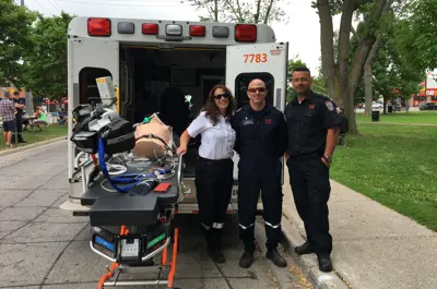 Three paramedics with a stretcher in front of the back of an open ambulance