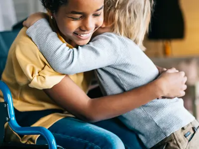 Young girl in a wheelchair getting a hug from her new friend at camp