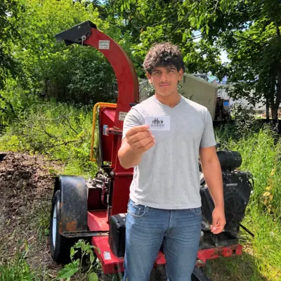 Young man standing in front of some landscape equipment holding up a business card.