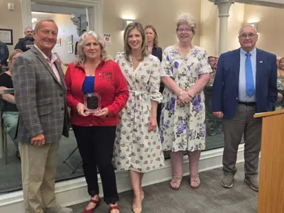 Photo of five people posed as one holds an award.