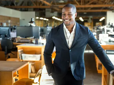 Man in suit standing and smiling in front of desks with computers