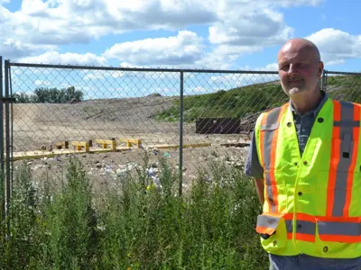 A city worker wearing a safety vest poses beside a fence outside the Linsday landfill