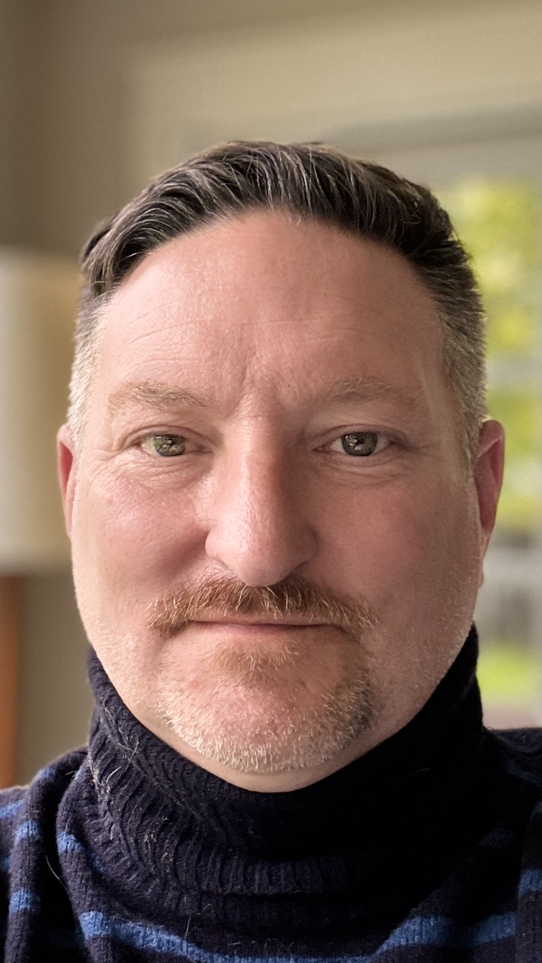 Adult male headshot, wearing dark blue turtleneck.
